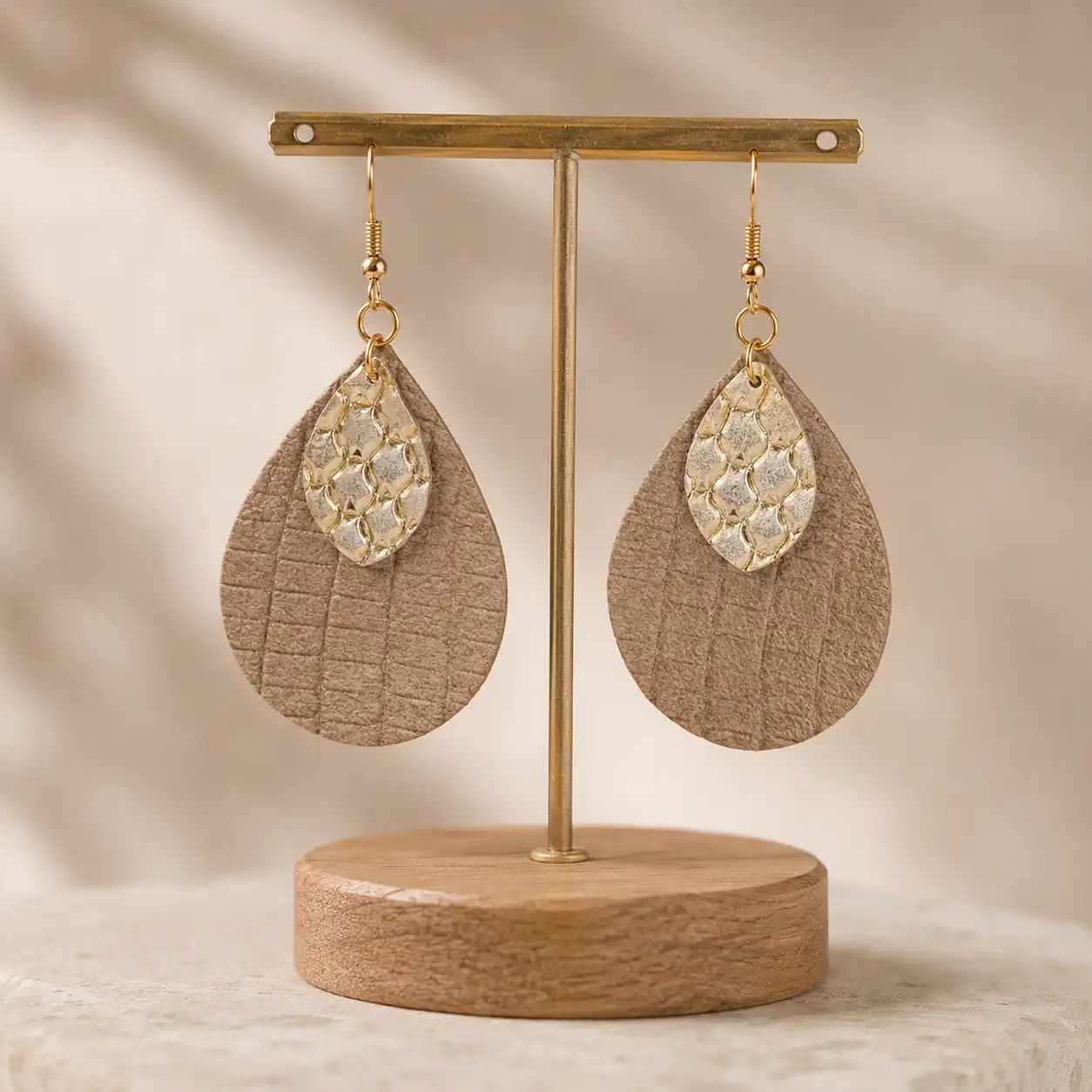 Boucles d'oreilles artisanales en cuir beige taupe et doré suspendues sur un présentoir