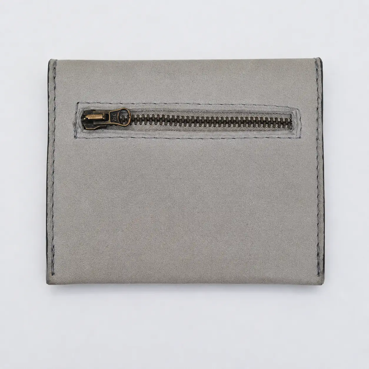 Dos d'un porte-monnaie artisanal en cuir gris clair, piqûre grise, avec poche zippée extérieure